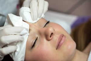 cara de mujer retirando el producto de un alisado de cejas con ayuda de algodón
