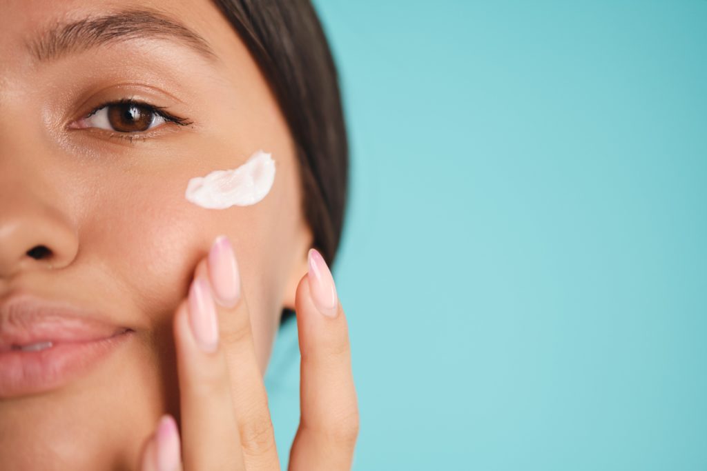 chica aplicando crema en su mejilla